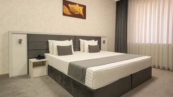 Ein Hotelzimmer mit einem großen Bett, einem Nachttisch, einem Wandbild und einem Fenster mit Vorhängen.