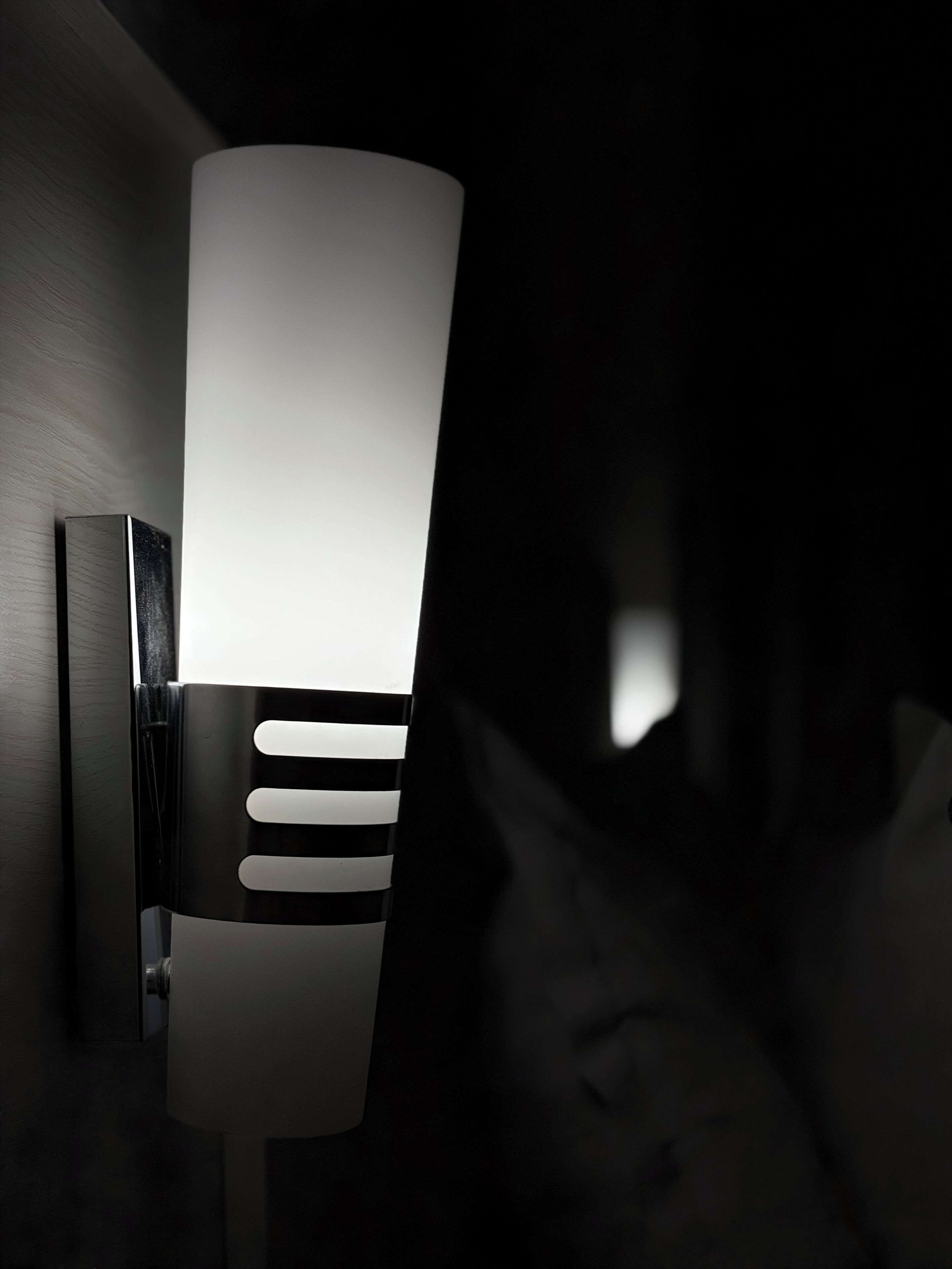 A wall-mounted light fixture with a cylindrical shade and horizontal slats.