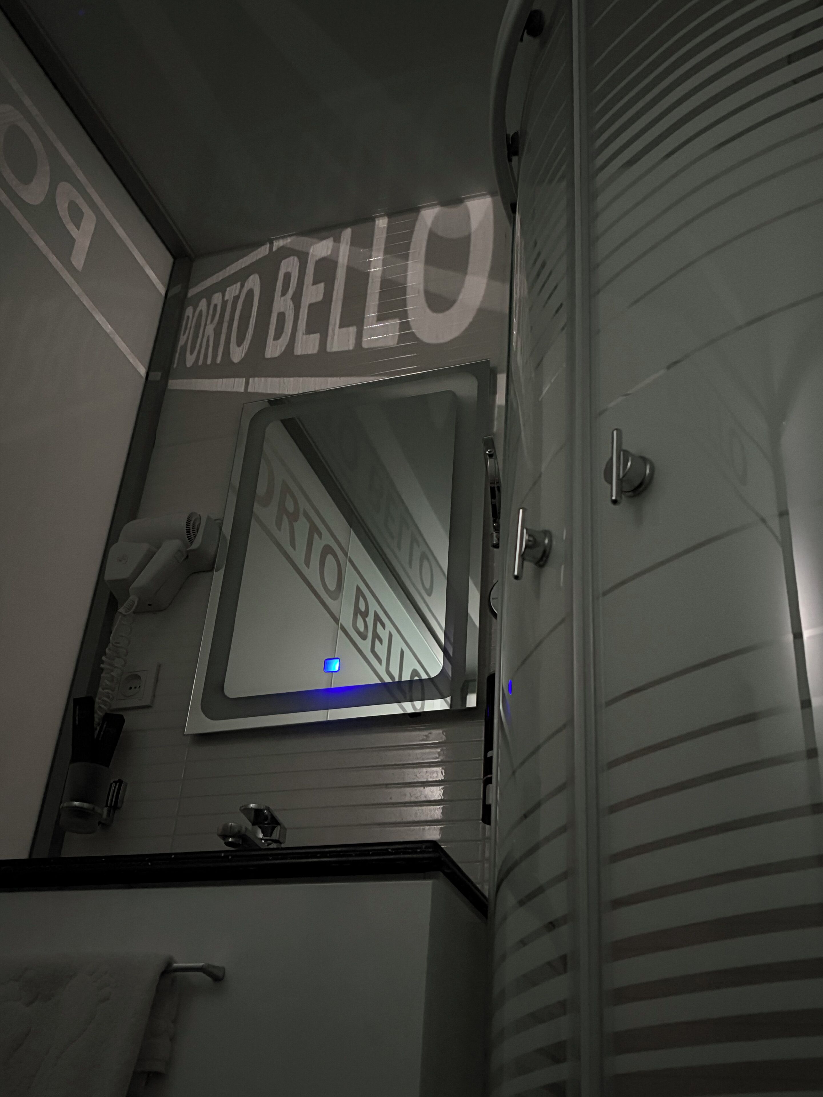 A bathroom with a mirror, a towel rack, and a sign that reads 'PORTO BELLO'.