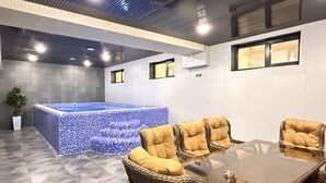 Een wellnessruimte met een jacuzzi, rieten meubels en een betegelde vloer.