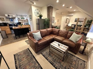A modern living room with a brown leather sectional sofa, a small side table, and a patterned rug. - Claim this entire luxury harbor-view cottage at 12 Goodwin St in Yachting Village! Complete with kitchen, private decks with water views, mini-split AC, TVs, Wifi and off-street parking. Steps to harbor, Thames Street, restaurants - Relax & Enjoy! (Newport)