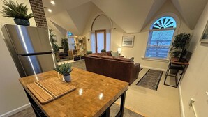 Eine Küche mit Holzausziehtisch, einem Edelstahlkühlschrank und einem Essbereich mit einer braunen Ledersofa.