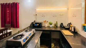 A compact kitchen with a gas stove, a microwave, and a coffee maker. There are cabinets, a sink, and a countertop with various kitchen items. - CELESTE VILLA (Candolim)