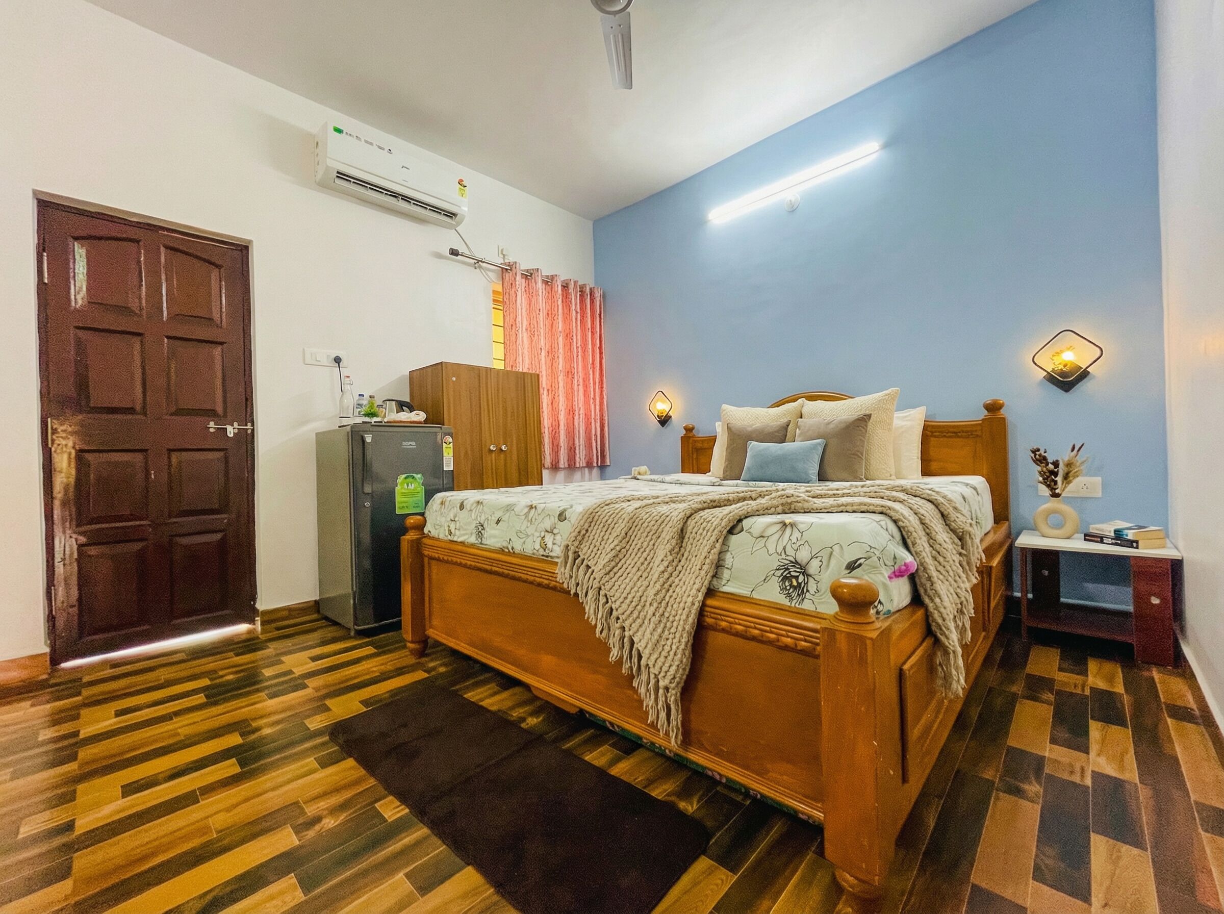 Un dormitorio con una cama de madera, un armario, un refrigerador, una mesita de noche con lámpara y aire acondicionado instalado en la pared.