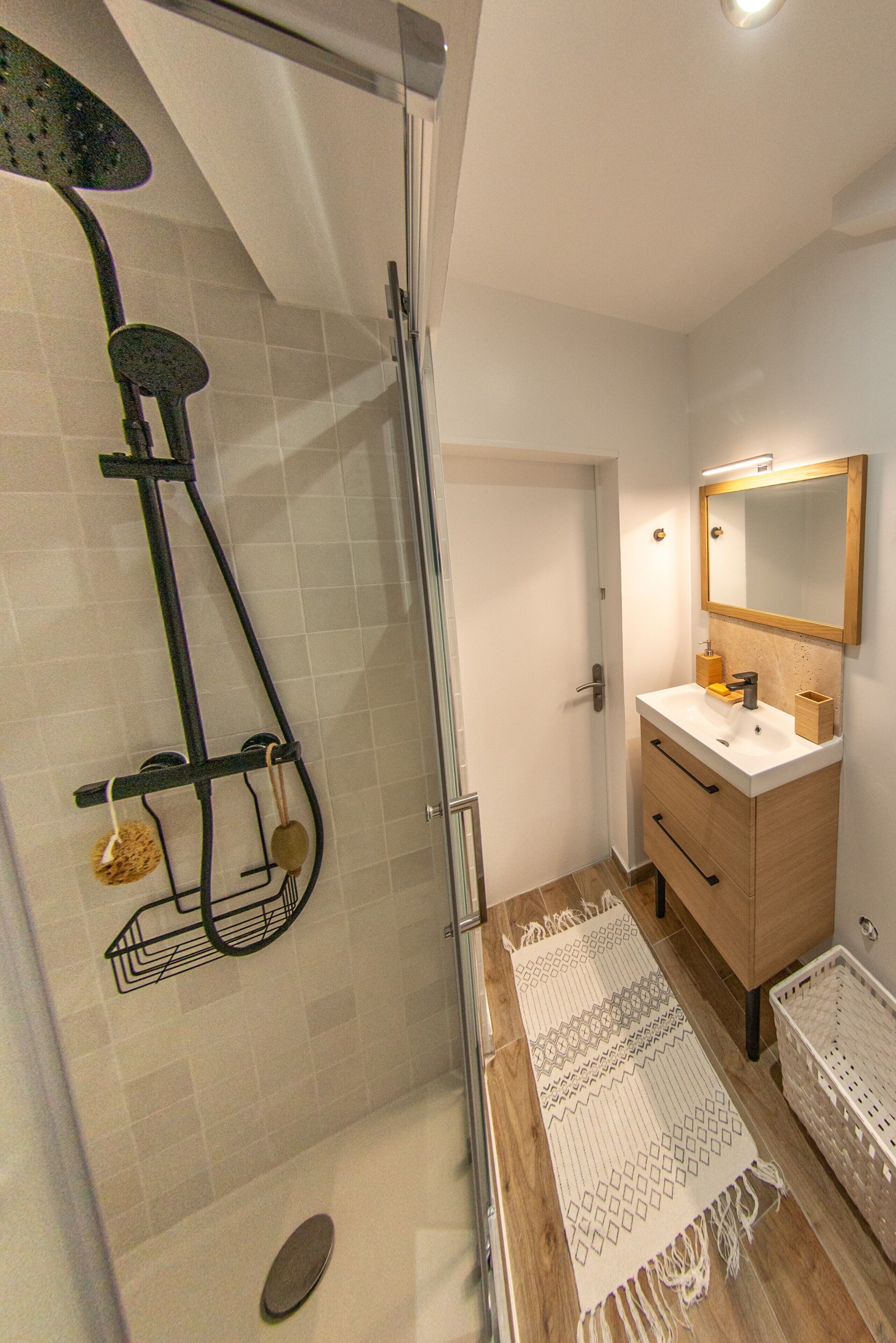 A bathroom with a shower, a sink, a mirror, and a patterned rug.