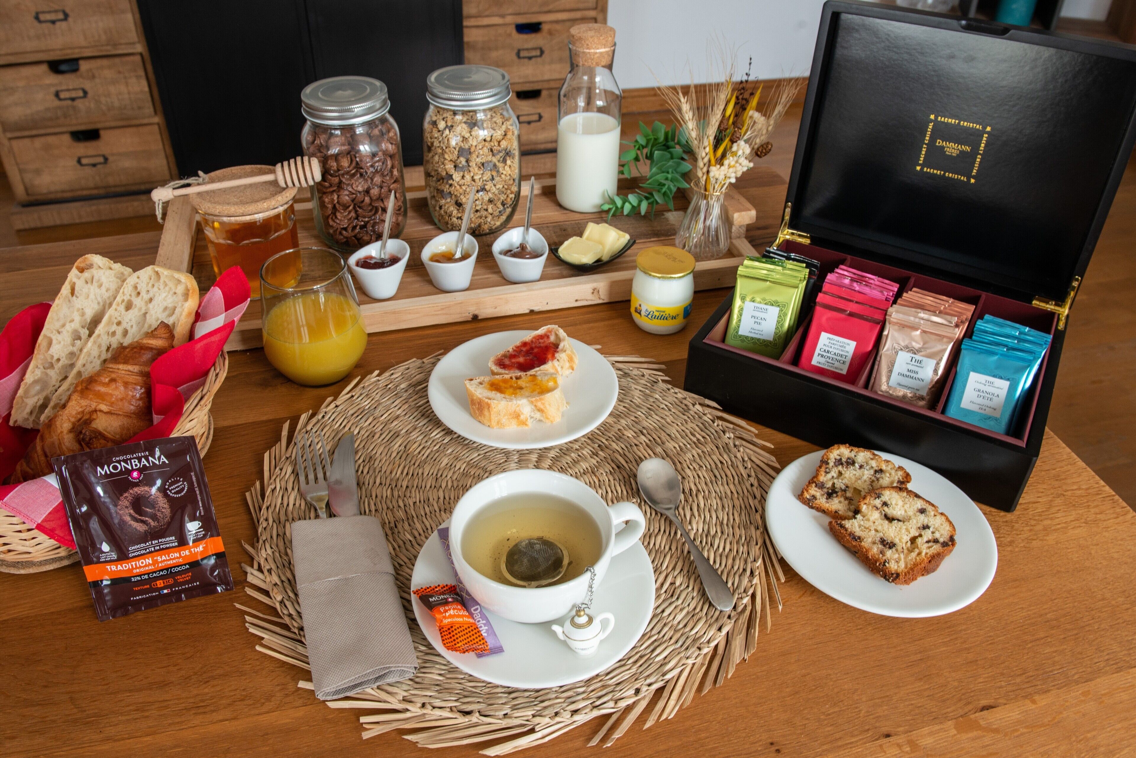 Un plateau de petit-déjeuner comprenant du pain, des viennoiseries, une théière et une boîte de chocolats.