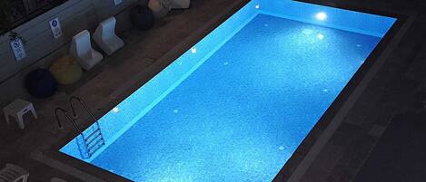 Una piscina rettangolare con bordo piastrellato, circondata da lettini e una piccola zona prendisole con ombrellone decorato.