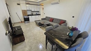 En moderne stue med sofa, spisebord og et køkken i baggrunden.