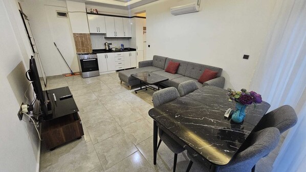 A modern living room with a sofa, a dining table, and a kitchen in the background.