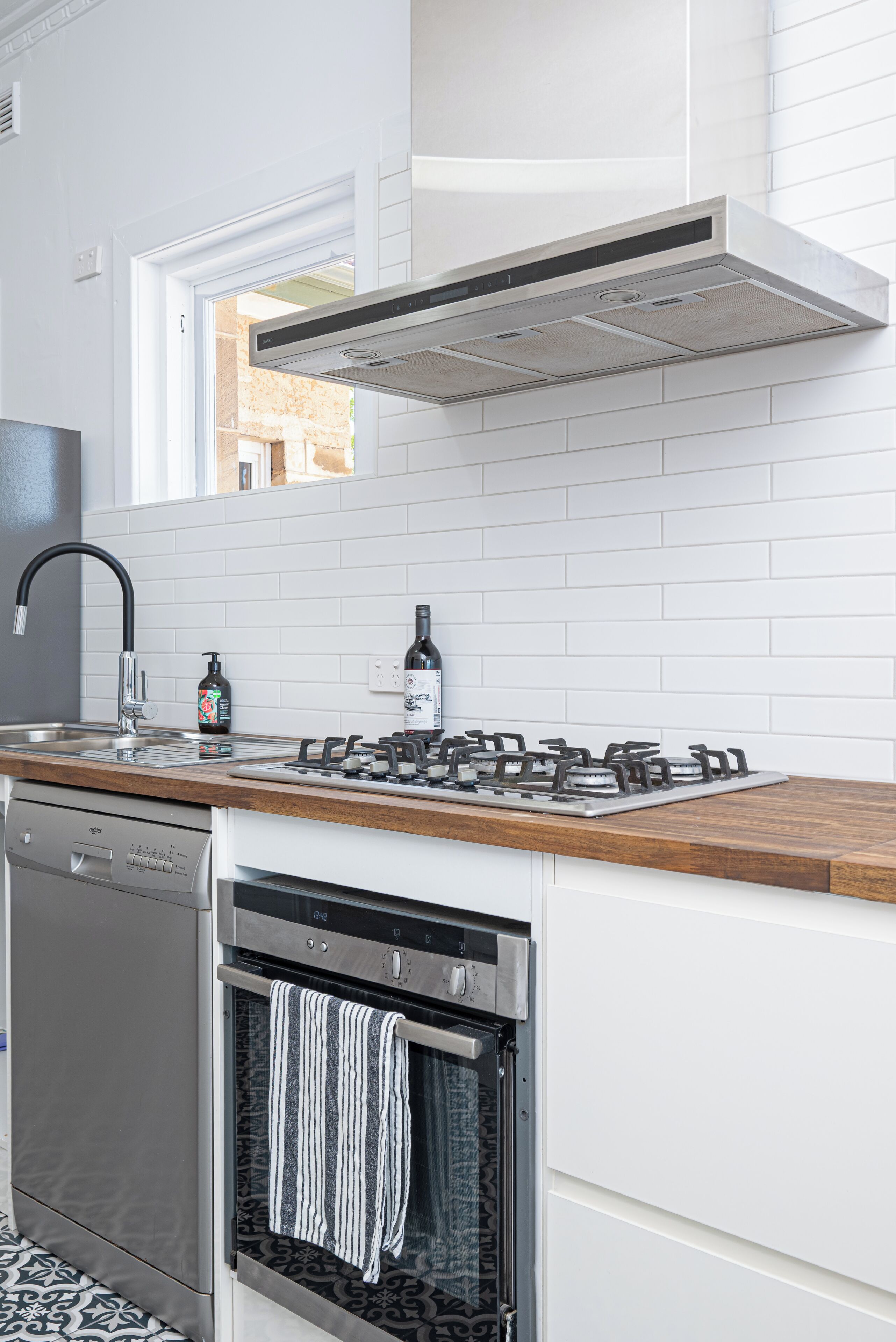 Eine moderne Küche mit weißen Schränken, einem Edelstahl-Geschirrspüler, einem eingebauten Backofen, einem Gasherd und einem Fenster über der Spüle.