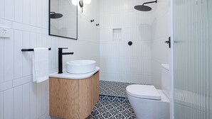 Een moderne badkamer met een houten wastafelmeubel, een wit toilet, een douche met een zwarte hendel en een spiegel met verlichting.