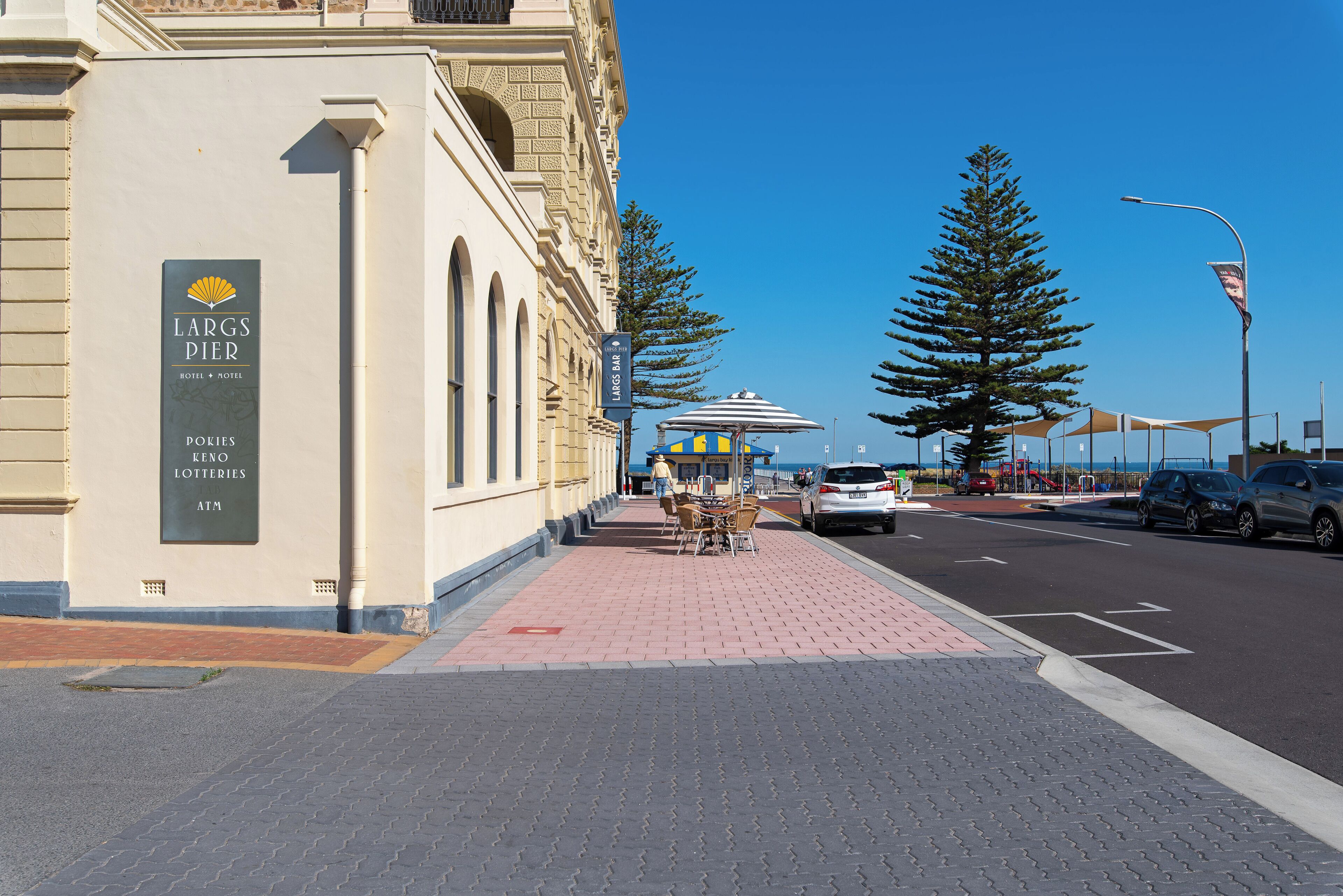 A building with a sign for LARGS PIER HOTEL & MOTEL, a kiosk with an umbrella, and a clear blue sky.