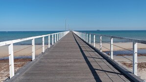 Een houten pier die zich uitstrekt in de zee, met witte relingen aan beide kanten.