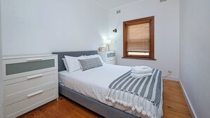 Een slaapkamer met een bed, nachtkastje, lamp en een raam met zonwering.