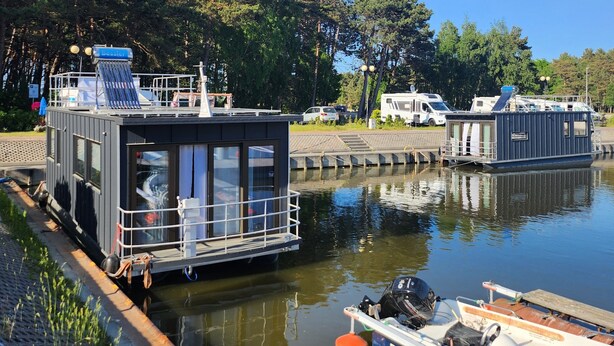 A narrow waterway with a houseboat docked on the left and a smaller boat on the right.