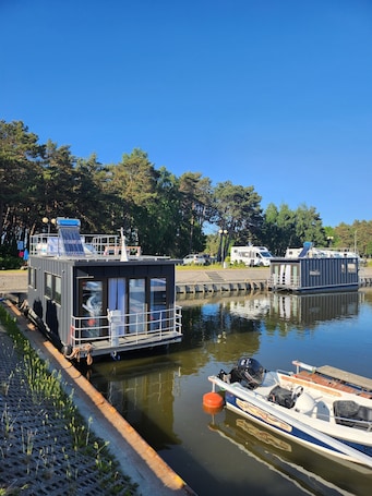 A narrow waterway with a houseboat docked on the left and a smaller boat on the right.. WOTELE PALLADIUM