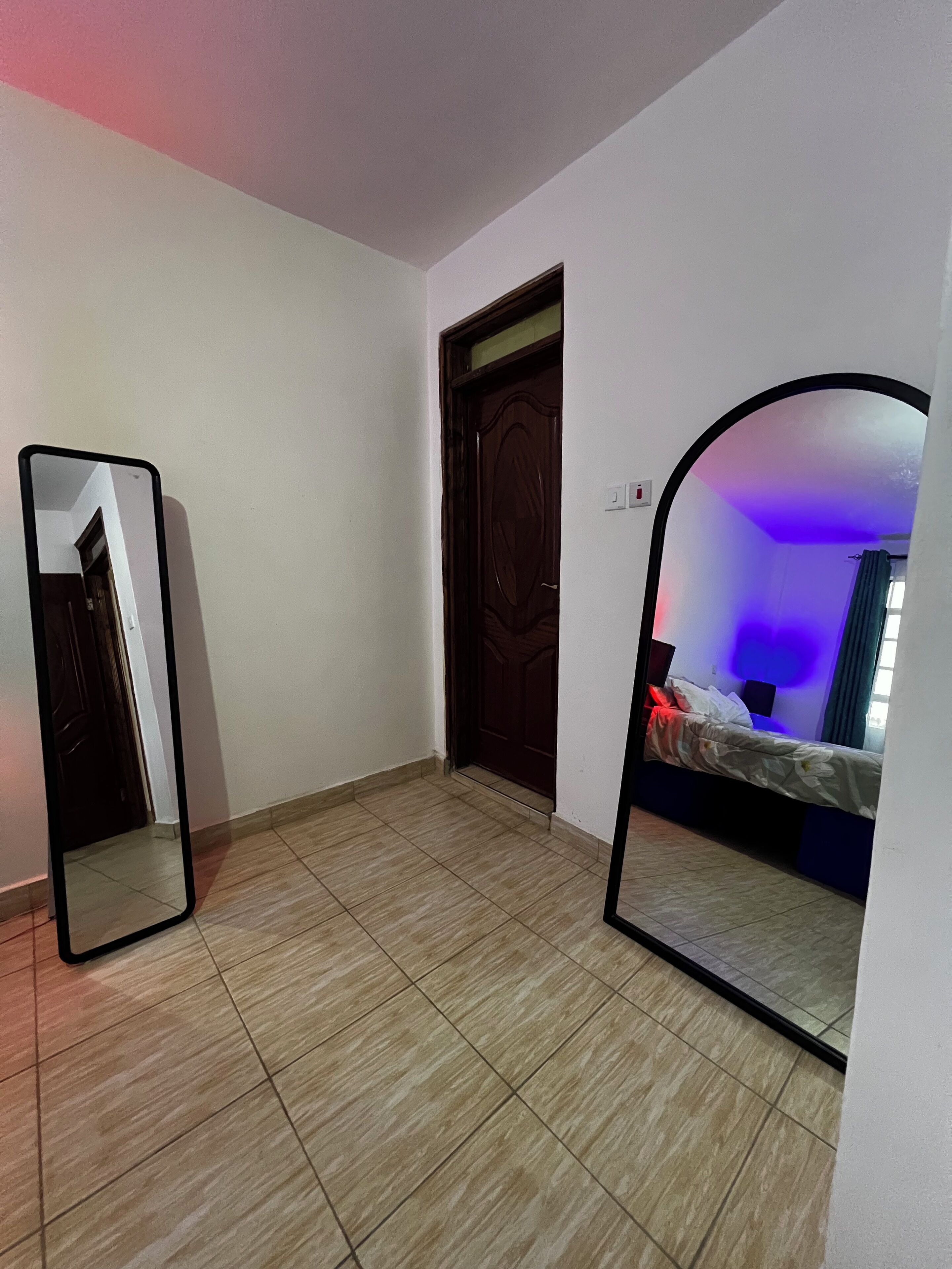 Une pièce avec un sol carrelé, une porte en bois, un lit avec une lumière bleue et un miroir au mur.
