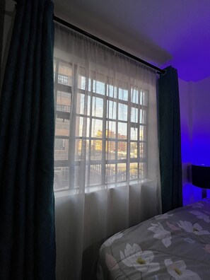A room with a bed, a window with sheer curtains, and a view of buildings outside. - Tulivu Homes, cozy 1-bedroom apartment in Utawala, Eastern Bypass, Nairobi. (Nairobi)