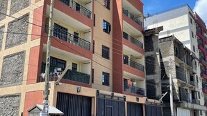 Un edifici de diverses plantes amb balcons, una entrada tancada per una reixa i un cotxe vermell a la part frontal.