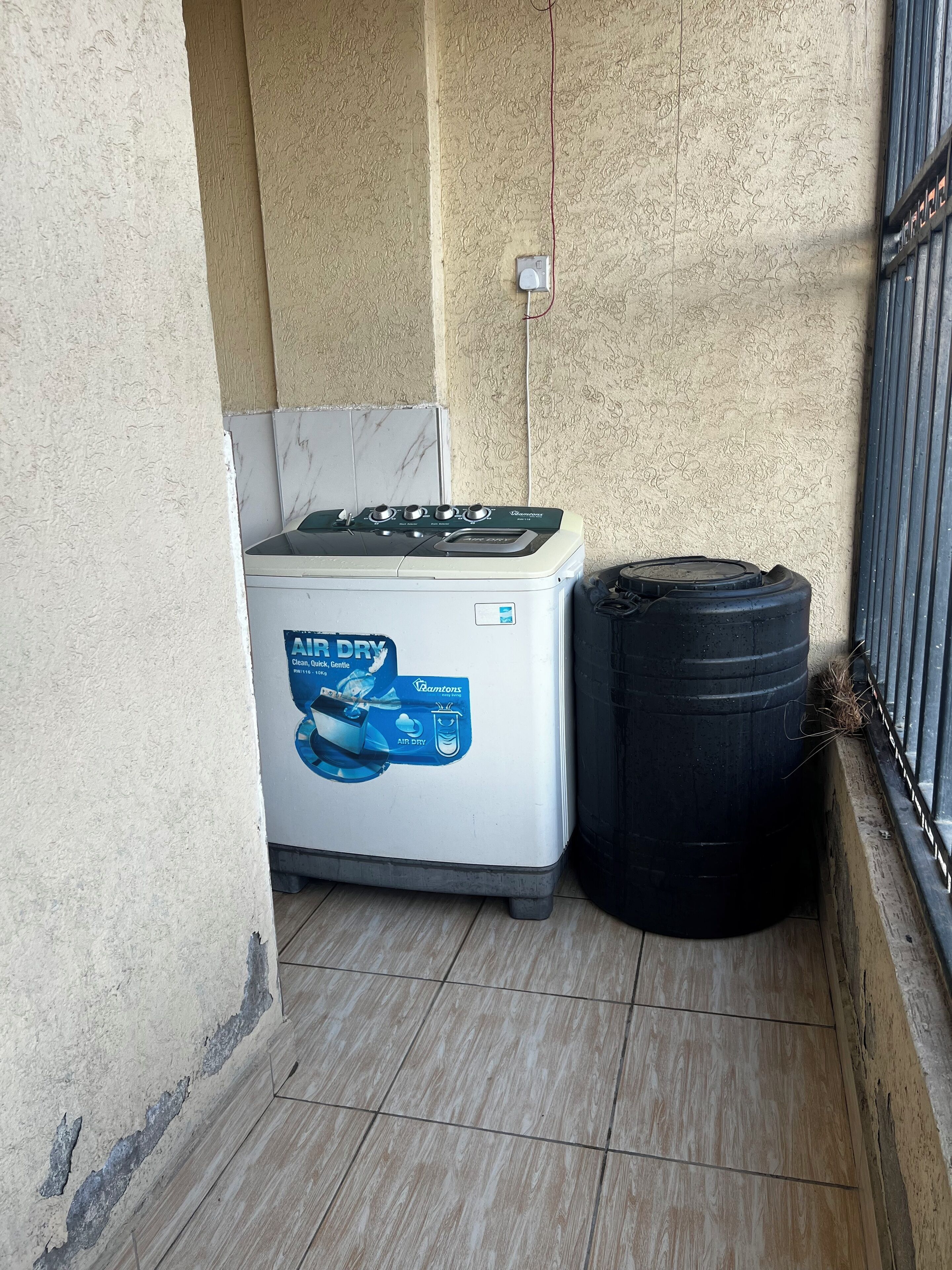 Een wasmachine en een zwarte vat in een hoek, met betegelde muren en een metalen leuning.