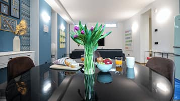 Una mesa de comedor con un jarrón de tulipanes, un cuenco de fruta y un vaso de jugo de naranja.