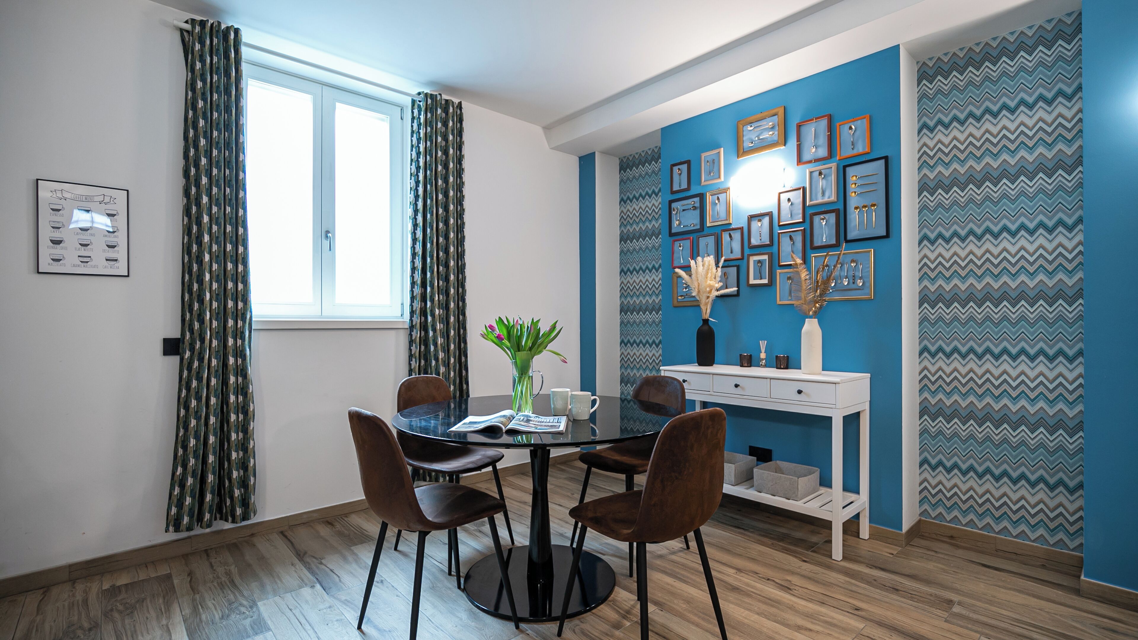 Un coin repas comprenant une table ronde, quatre chaises, un vase avec des fleurs et un mur orné de tableaux encadrés.