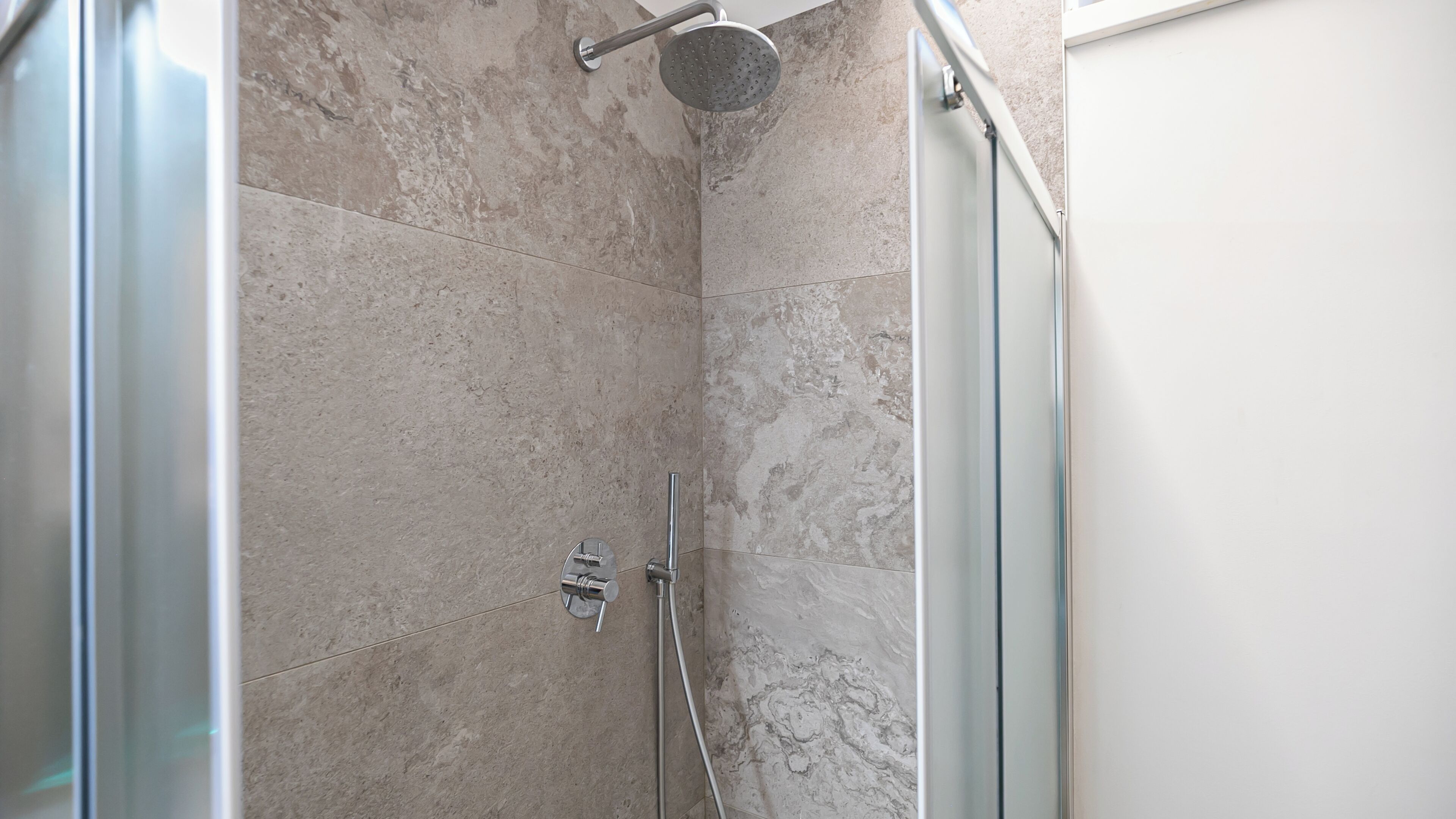 A modern shower with a handheld showerhead and a wall-mounted faucet.