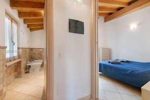 Ein Schlafzimmer mit Bett, ein Badezimmer mit Toilette und Waschbecken sowie eine Holzbalkendecke.