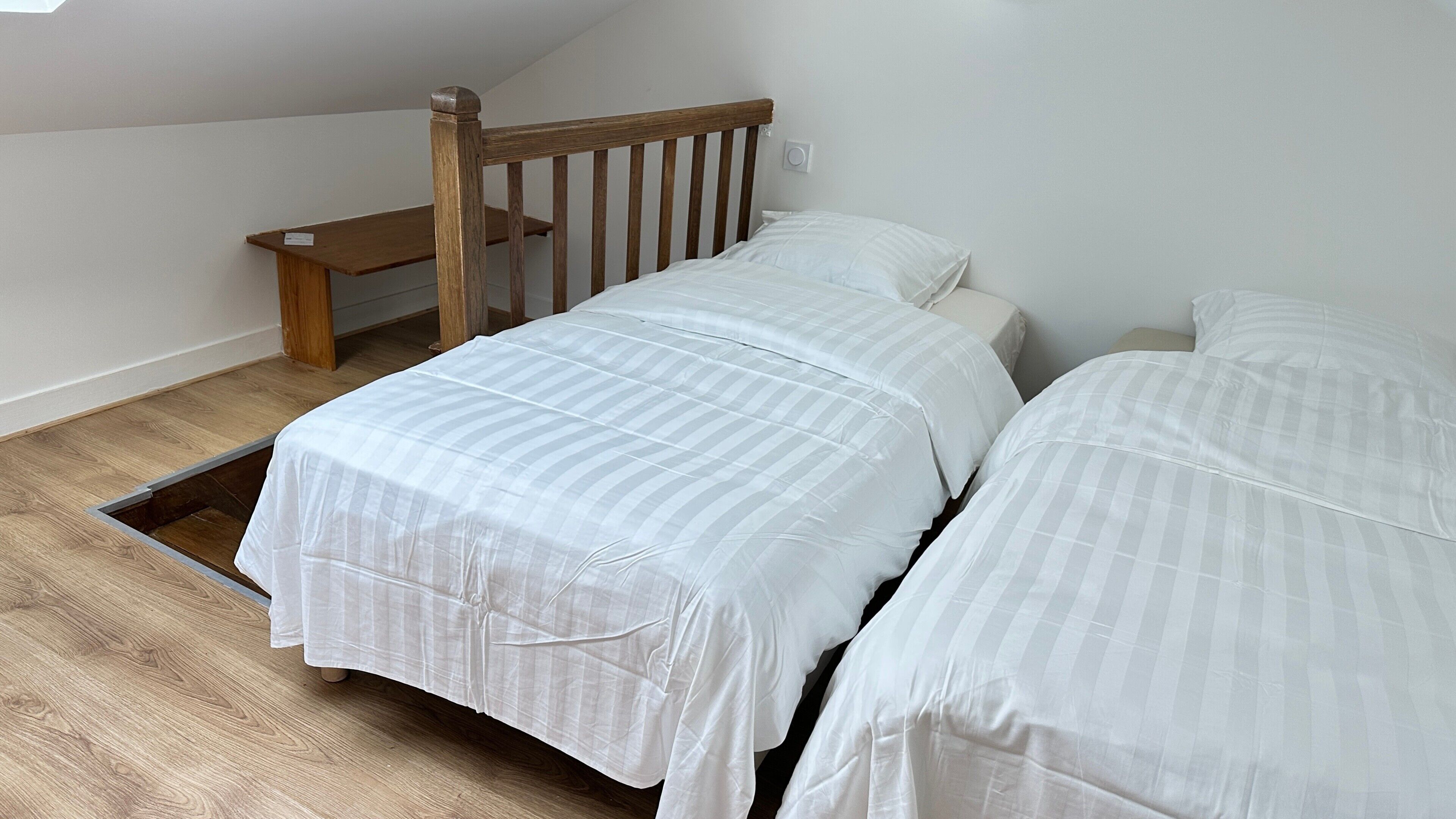 A bedroom with two beds, a wooden headboard, a small wooden table, and a skylight.
