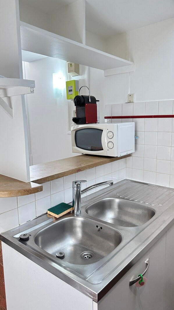 A kitchen with a double sink, a microwave, and a small refrigerator.