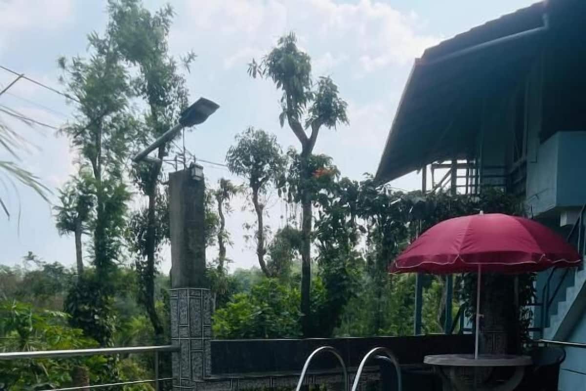 A swimming pool with a stone wall and metal railings, surrounded by lush greenery and a red umbrella.