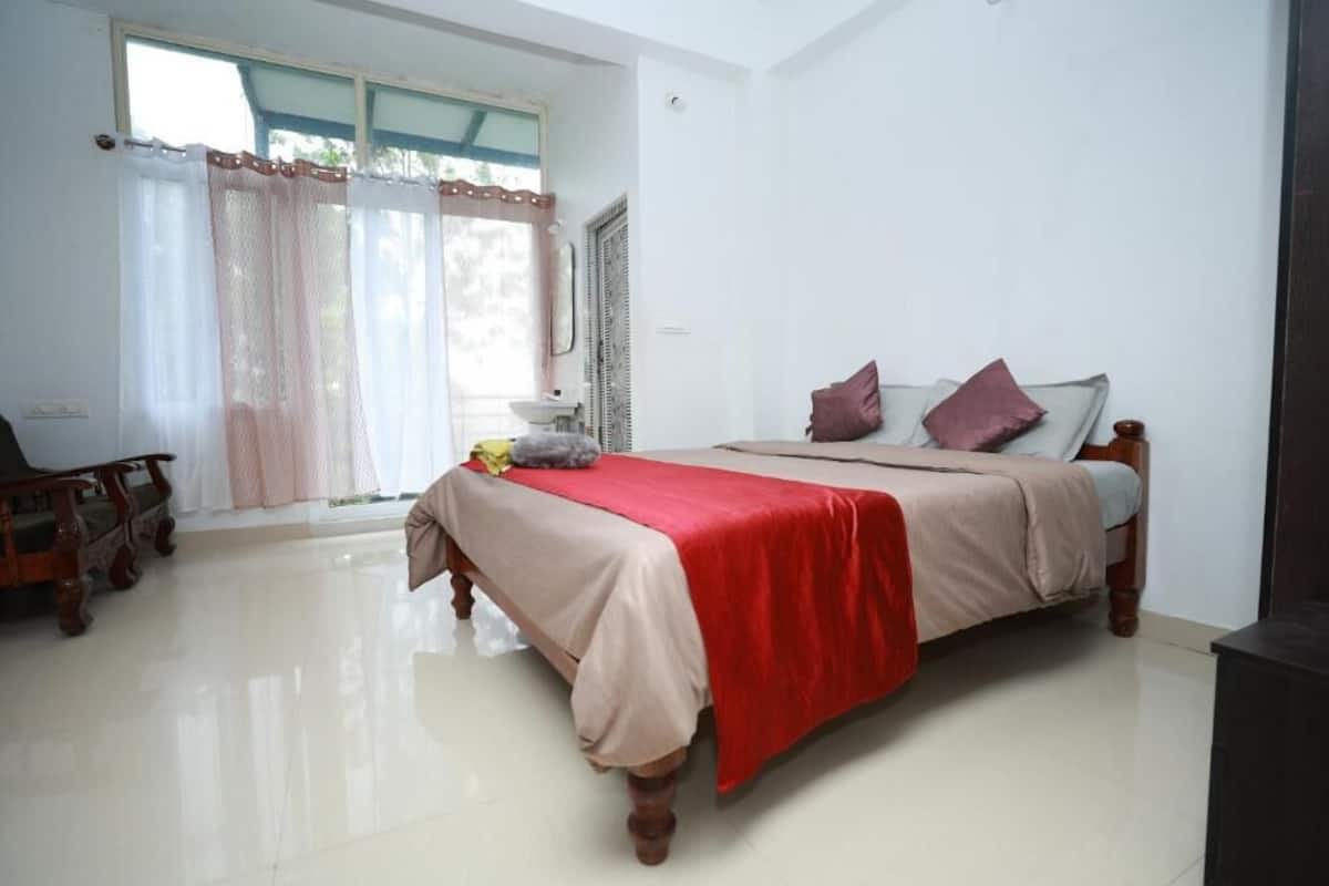 A bedroom with a bed, a chair, a window with curtains, and a sink.