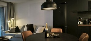 Ein modernes Wohnzimmer mit einer Couch, einem Esstisch mit einer Champagnerflasche und einer Küchenzeile mit Weinflaschen.