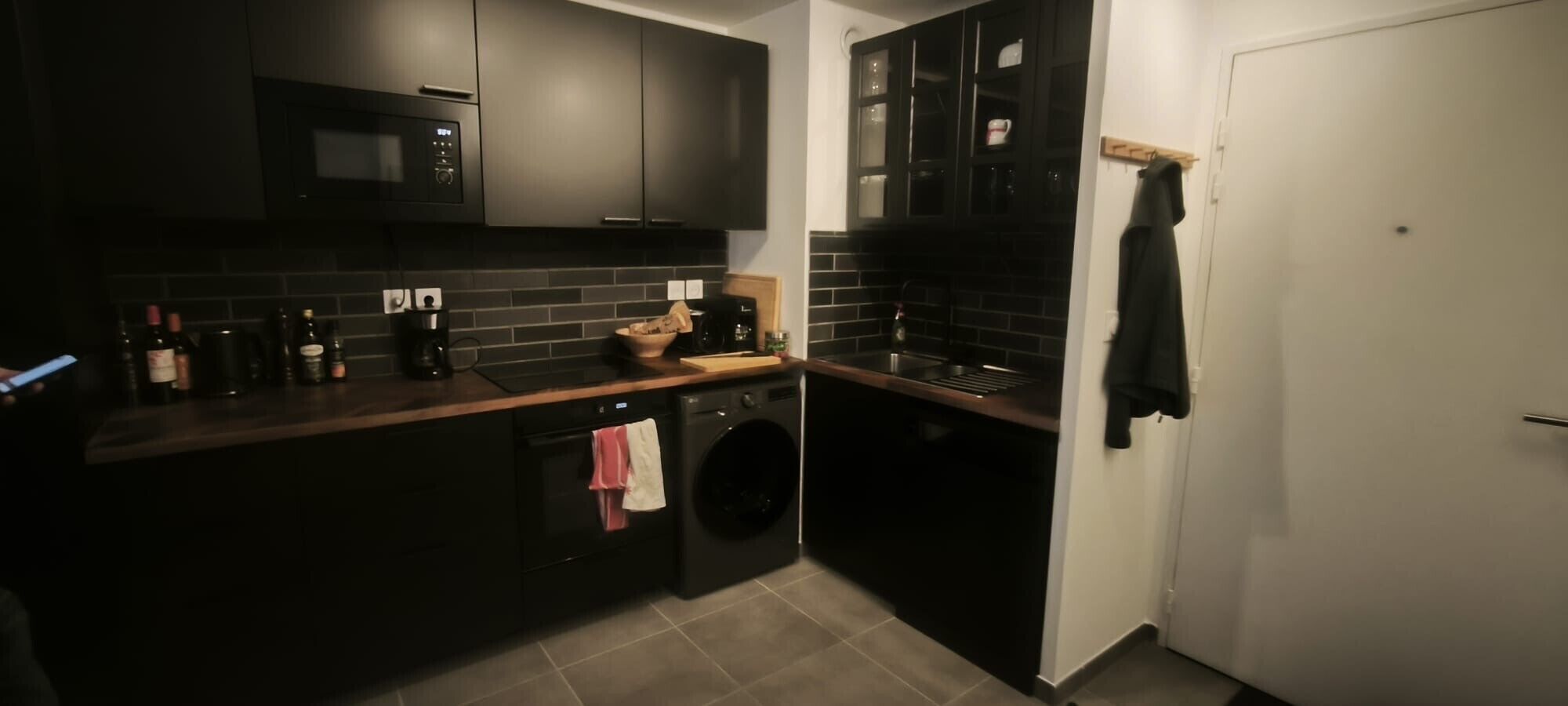 Una cocina moderna con armarios oscuros, microondas integrado, cafetera y lavadora.