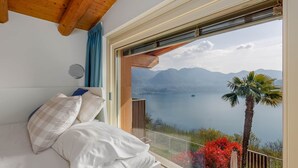 Camera da letto con una grande finestra, un letto con biancheria bianca e vista su un lago e montagne.