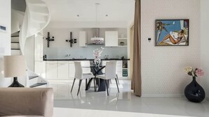 Una cucina moderna con mobili bianchi, un'area pranzo con tavolo in vetro e un quadro appeso al muro.