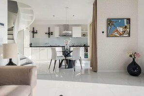 A modern kitchen with white cabinets, a dining area with a glass table, and a painting on the wall. - IseoLake Places - Casa Aria (Spiglia)