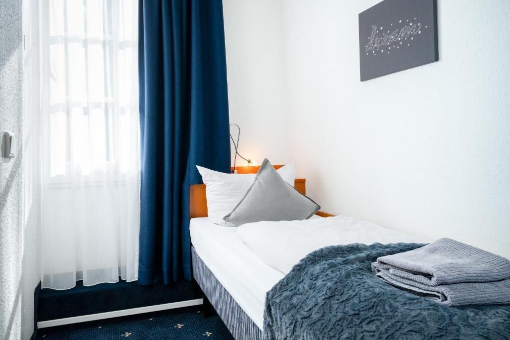 A neatly made bed with white bedding and a grey throw blanket, a bedside lamp, and a wall-mounted picture frame.