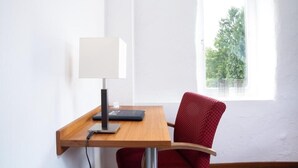 A corner room with a desk, chair, lamp, and a window with a view of trees.