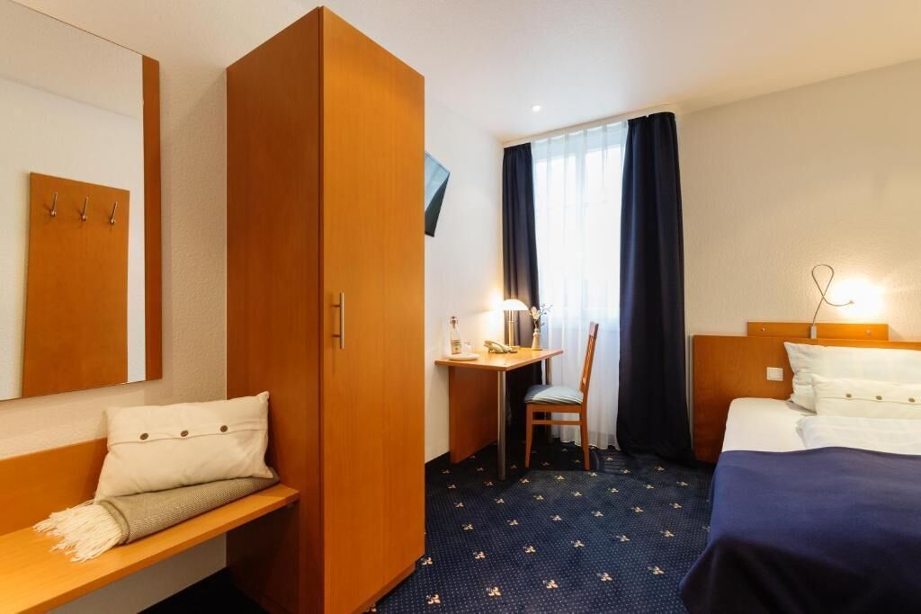Una camera d'albergo con un letto, una scrivania, una sedia, un armadio e una televisione.