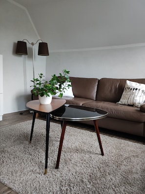 Ein modernes Wohnzimmer mit einem braunen Ledersofa, einem runden Couchtisch mit einer weißen Pflanze und einer hohen Stehlampe.