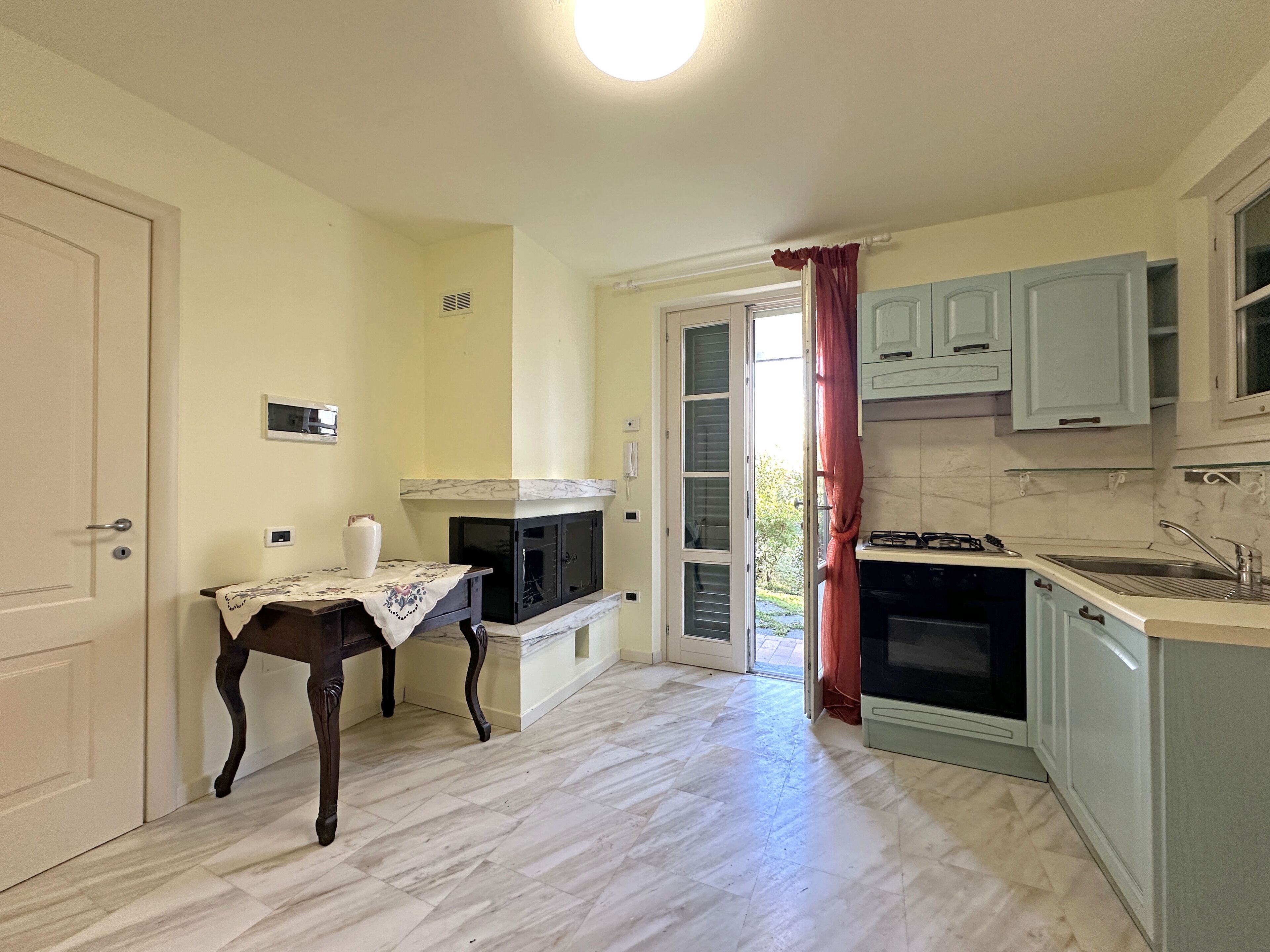 A kitchen with a marble countertop, a built-in oven, and a window with a curtain.