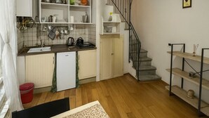 A compact kitchen with white cabinets, a sink, and a stove. There's a staircase leading to a loft area with a wooden railing. - Charming Studio Apartment in Lucca in the Historic Center - BanStay (Lucca)