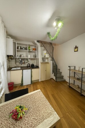 A compact kitchen with white cabinets, a sink, and a stove. There's a staircase leading to a loft area with a wooden railing. - Charming Studio Apartment in Lucca in the Historic Center - BanStay (Lucca)