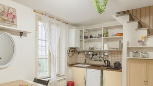 A compact kitchen with wooden flooring, a dining table with chairs, a small refrigerator, and a staircase leading to an upper level. - Charming Studio Apartment in Lucca in the Historic Center - BanStay (Lucca)