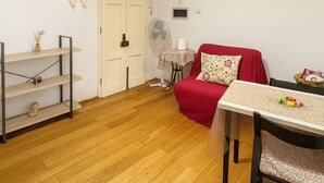 A compact living space with a dining table, a red sofa, a wooden floor, and a white door. - Charming Studio Apartment in Lucca in the Historic Center - BanStay (Lucca)