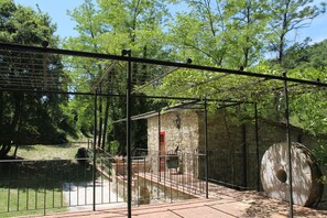 A stone building with a red door, a metal fence, and a large tree trunk. - The small mill on the Argenna stream in the woods of Chianti in Tuscany (Toscana)