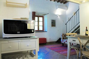 A compact living space with a microwave on a white cabinet, a red bench, a patterned sofa, and a staircase leading upstairs. - The small mill on the Argenna stream in the woods of Chianti in Tuscany (Toscana)