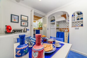 A dining area with a table set for two, featuring blue and white tableware, a red and blue bottle, and a white refrigerator in the background. - Estate4home - Le vele (Positano)