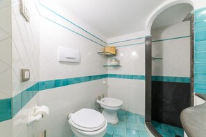 A bathroom with white and teal tiles, a toilet, a bidet, and a shower area. - Estate4home - Le vele (Positano)